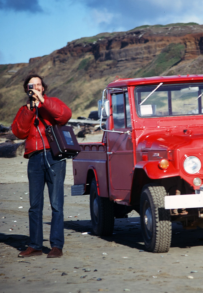 Photo of Bill Bradley with video recording equipment standing next to red Toyota truck on Whiskey Run Beach.
