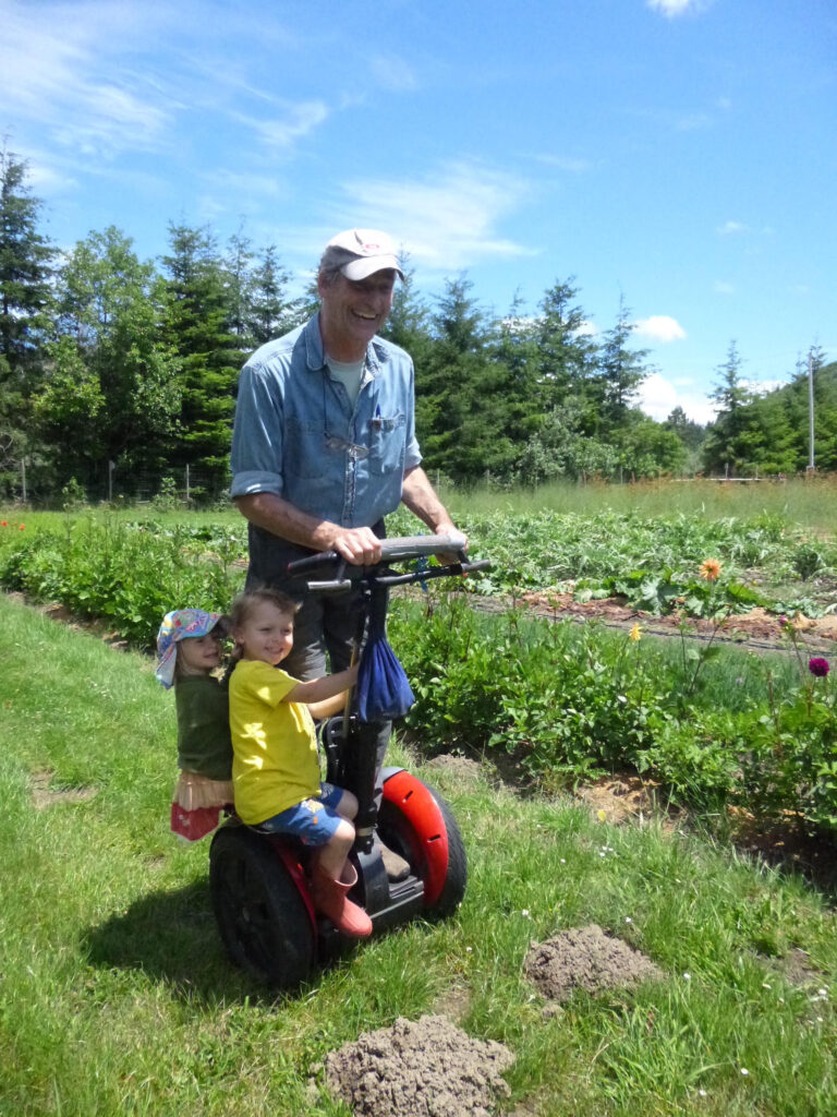 Photo of Bill Bradbury with two grandchildren at a farm riding on a Segway